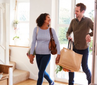 A man and a woman return home with shopping bags