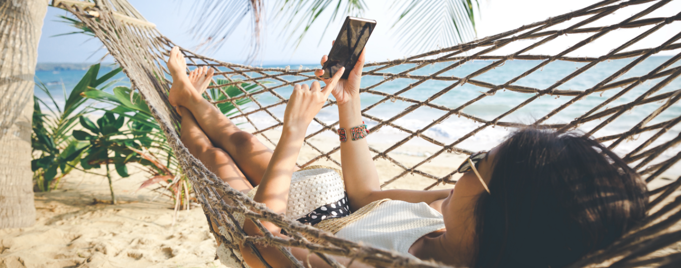 Kobieta leży na hamanku na plaży i korzysta ze smartfonu