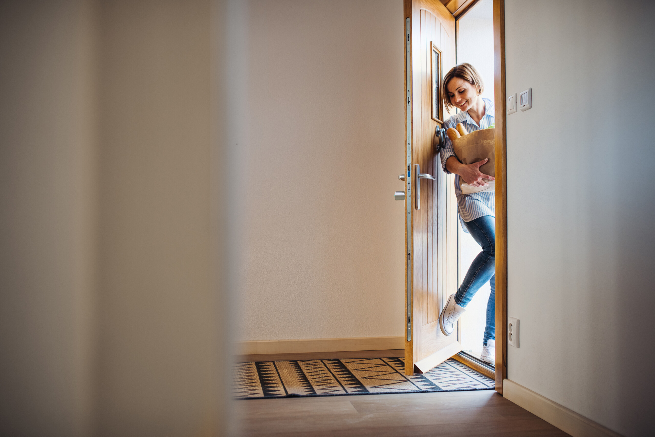 A woman with groceries in paper shopping bag walking in through the door