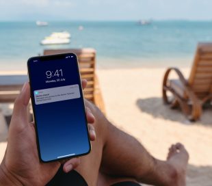 Mężczyzna siedzący na plaży otrzymuje powiadomienie na smartfon