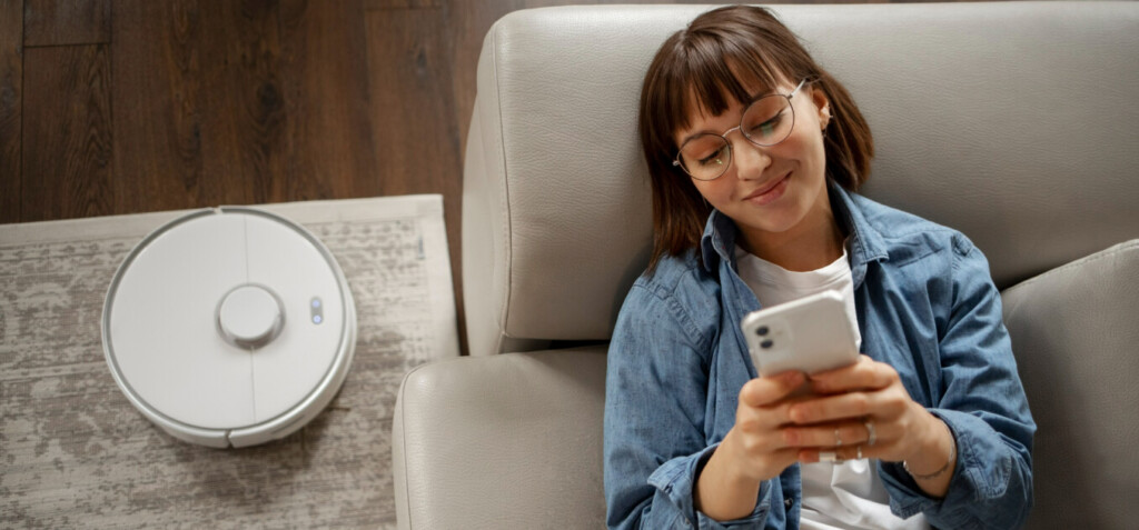 Lying on the couch, a woman sets up a smart vacuum cleaner using a smartphone