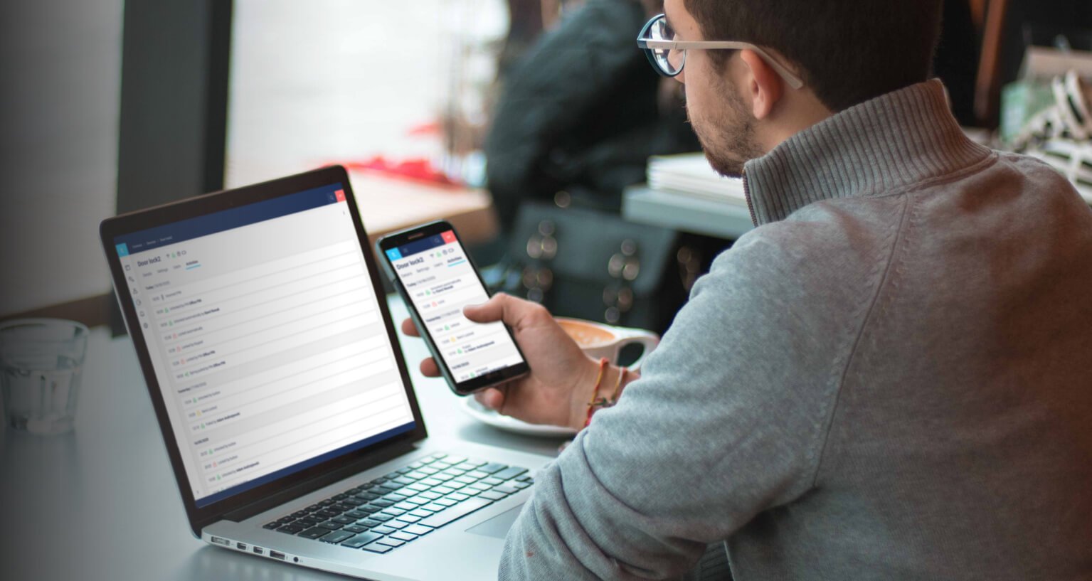 A man working on a laptop and holding a smartphone in his hand