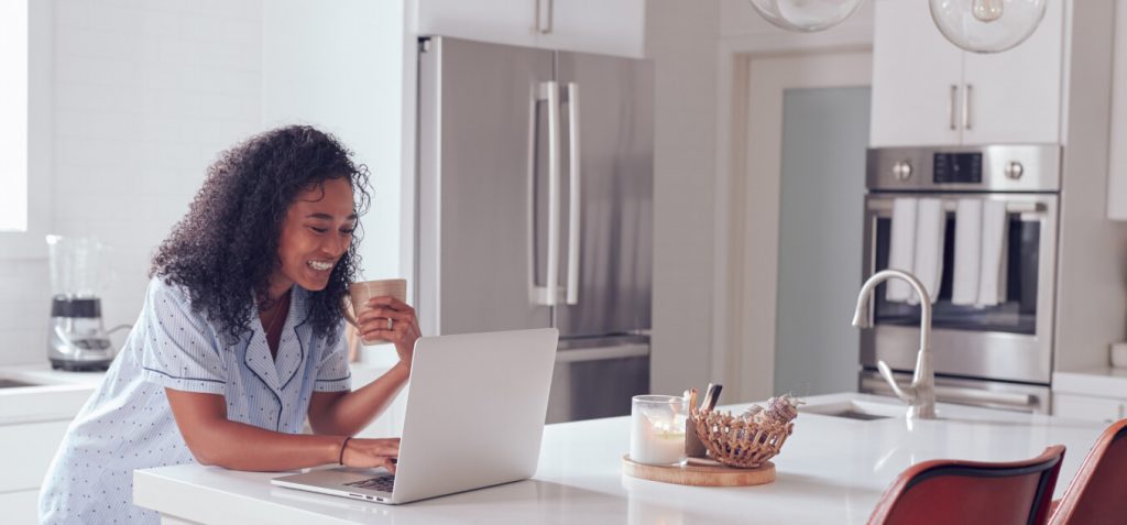 happy woman drinks her morning coffee and uses her laptop