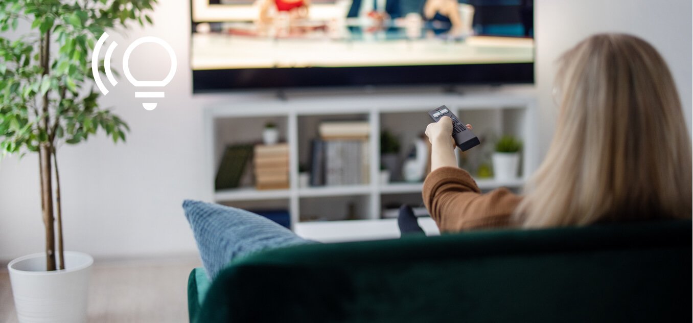a woman sitting on a sofa is using the remote control for the TV